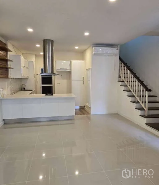 Townhouse for sale in Watthana, Bangkok - Modern kitchen with island cooktop, range hood and recessed lighting.