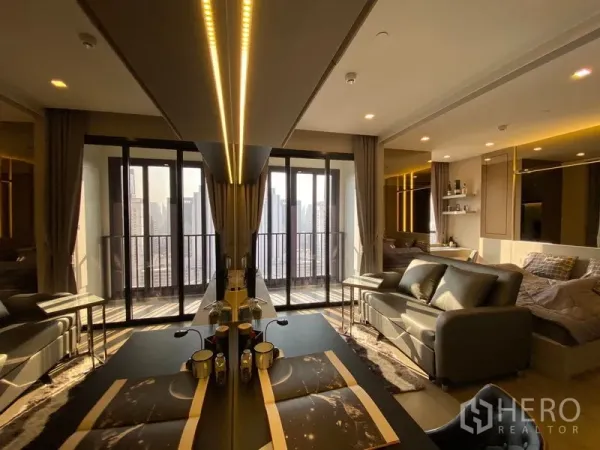 Condominium for rent in Watthana, Bangkok - Open-plan condo with dining table and sofa facing a wide balcony, warm cove lighting, and panoramic skyline view.