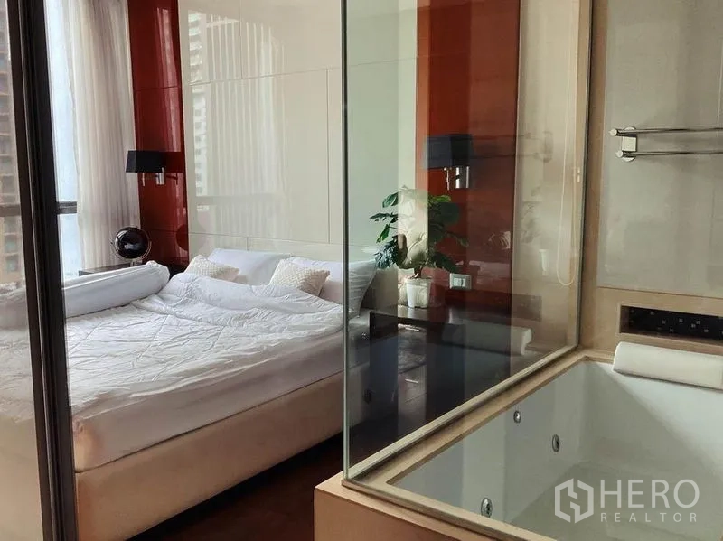 Condominium for rent in Khlong Toei, Bangkok - Bedroom with king bed beside a glass partition to the bathtub area.