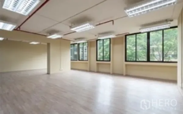 Office Space for rent in Chatuchak, Bangkok - Open-plan office with wood floors, multiple fluorescent lights, exposed red piping and large windows facing trees.