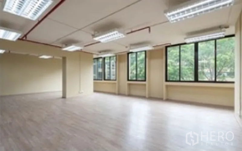 Office Space for rent in Chatuchak, Bangkok - Open-plan office with wood floors, multiple fluorescent lights, exposed red piping and large windows facing trees.