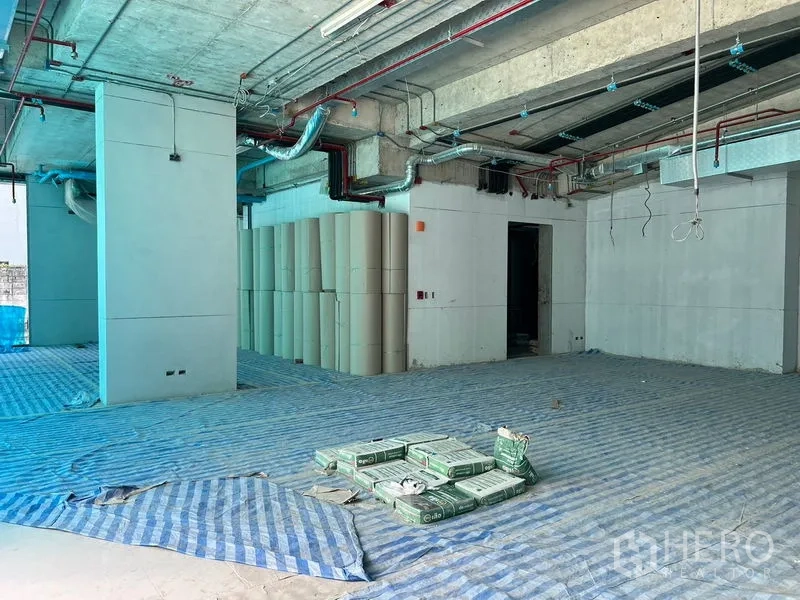 Retail Space for rent in Khlong Toei, Bangkok - Unfinished retail floor with columns, stacked supplies, and visible ceiling services.