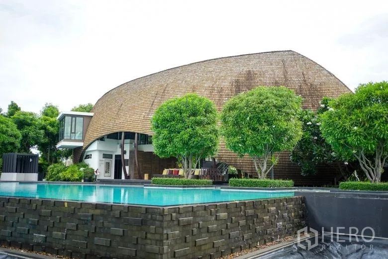 Detached House for rent in Sai Mai, Bangkok - Community clubhouse with a contemporary curved roof next to a raised outdoor swimming pool.