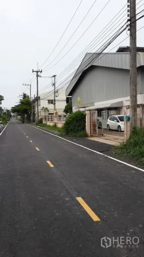 Factory for rent in Lat Lum Kaeo, Pathum Thani - Paved two-lane road beside a corrugated factory exterior with parking and power lines.