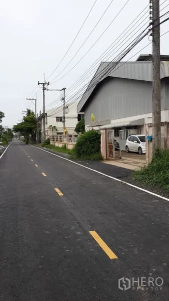 Factory for rent in Lat Lum Kaeo, Pathum Thani - Paved two-lane road beside a corrugated factory exterior with parking and power lines.