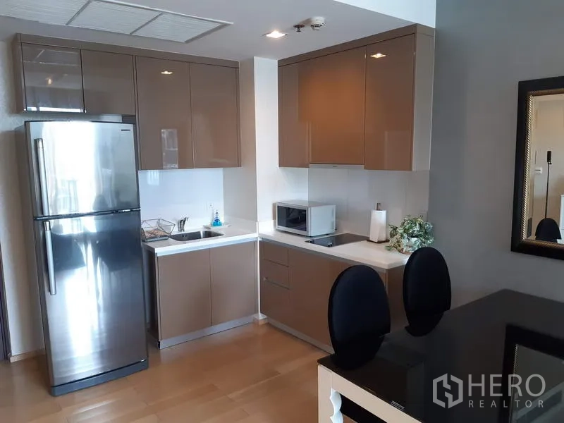 Condominium for rent in Khlong Toei, Bangkok - Modern L-shaped kitchen with glossy cabinets, stainless refrigerator, cooktop and microwave.