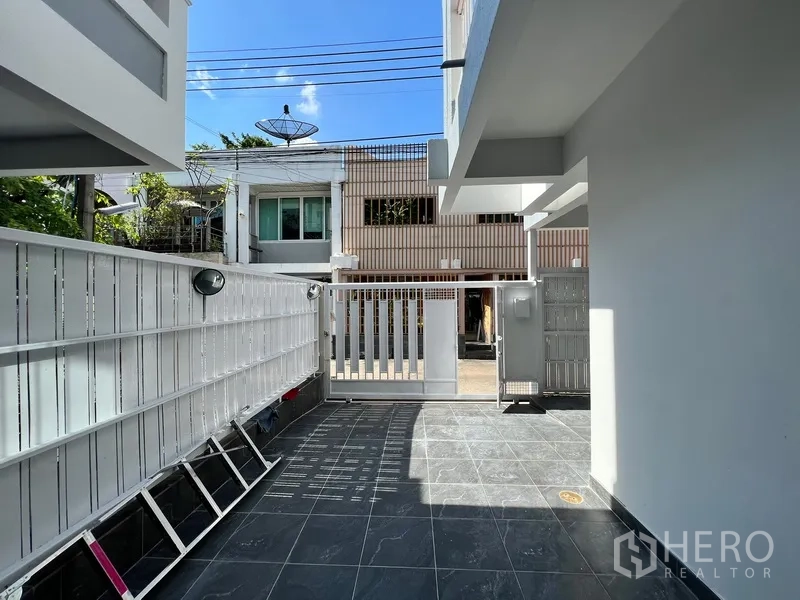 Home Office for rent in Watthana, Bangkok - Front courtyard with tiled driveway and secure metal gate, suitable for parking.
