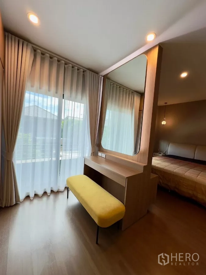 Detached House for rent in Samut Prakan - Vanity with mirror and bench beside sheer curtains leading to the balcony.