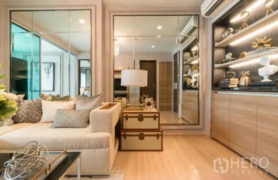 Condominium for rent in Sathon, Bangkok - Bright living room with L-shaped sofa, mirrored wall panels and built-in illuminated shelves.