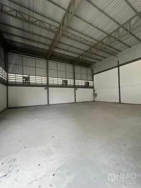 Warehouse for rent or sale in Sai Noi, Nonthaburi - Empty warehouse interior with high steel truss ceiling and smooth concrete floor.