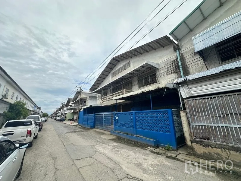 Factory for rent in Lam Luk Ka, Pathum Thani - Quiet industrial street lined with warehouses and parking outside the property.
