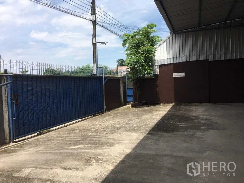 货栈 出租在Bueng Kum, Bangkok - 仓库前装卸庭院，蓝色滑动大门、围栏与局部遮棚。