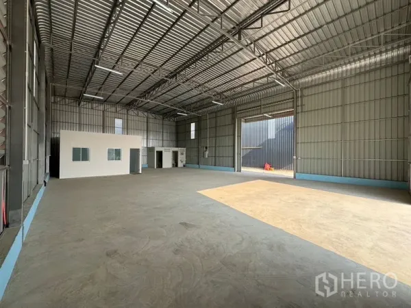 Warehouse for rent in Lam Luk Ka, Pathum Thani - Spacious warehouse interior with high steel-truss roof, large loading door and a small office box.