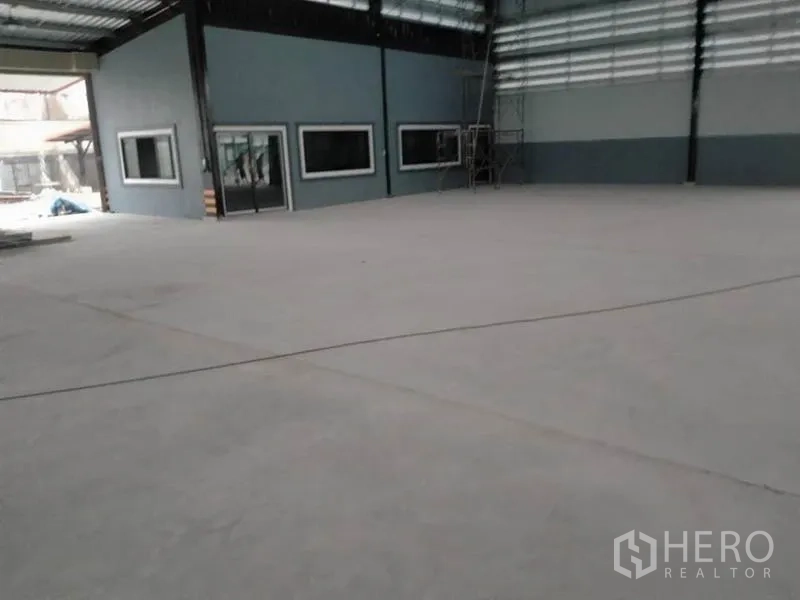 Factory for rent or sale in Phanat Nikhom, Chon Buri - Corner of the warehouse with office windows, scaffolding and smooth concrete flooring.