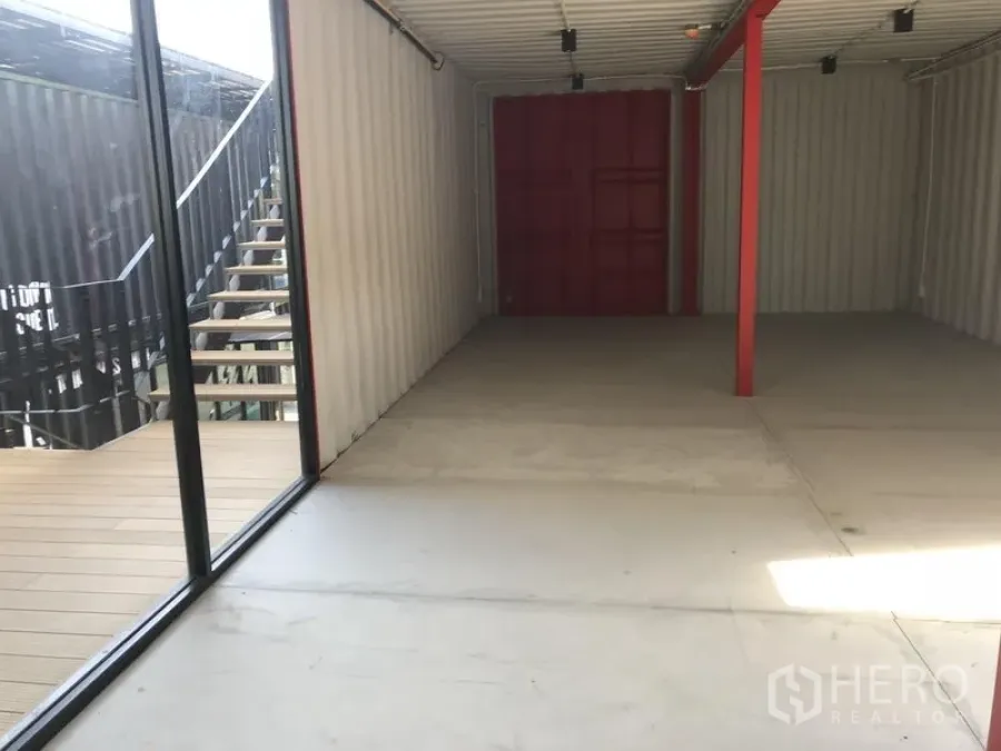 Office Space for rent in Khlong Toei, Bangkok - Open-plan container-style office with floor-to-ceiling glass, deck and exterior staircase, concrete floor and red steel beam.