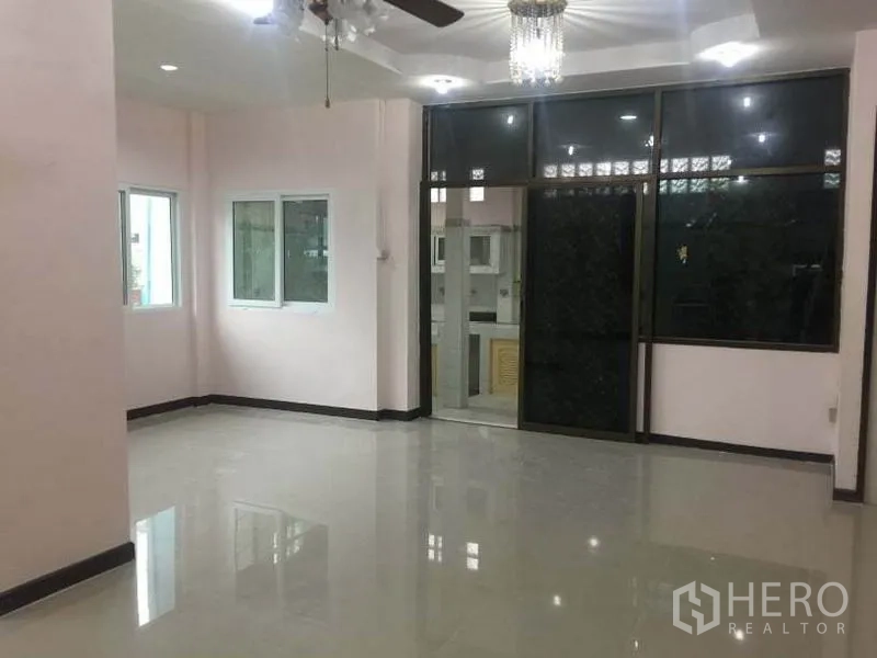 Detached House for rent in Chatuchak, Bangkok - Spacious living room with glossy tiles, ceiling fan and glass partition to the kitchen.