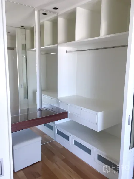 Condominium for rent in Khlong Toei, Bangkok - Spacious walk-in closet featuring white built-in cabinetry, drawers, mirrors and a dressing table.