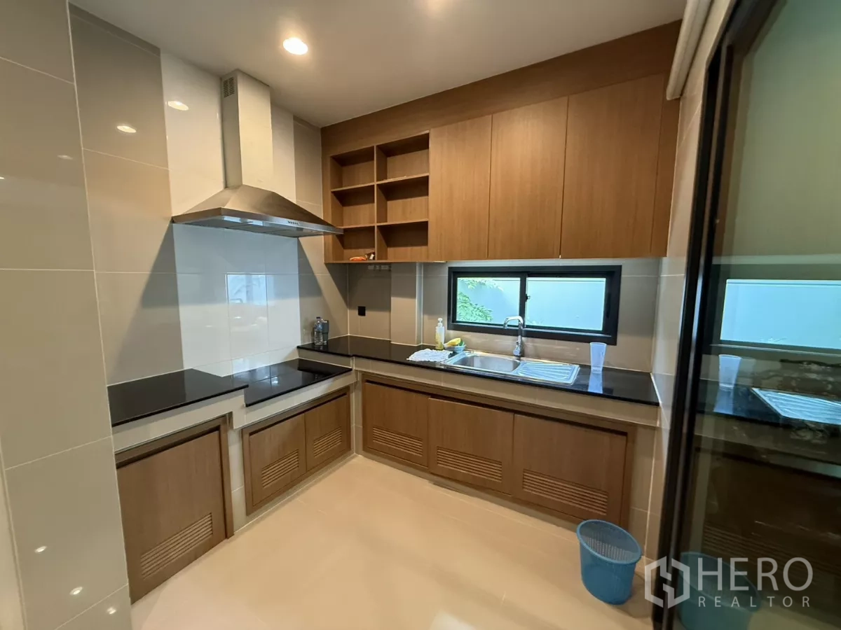 Detached House for rent in Bang Kapi, Bangkok - Built-in U-shaped kitchen with stone countertops, window, shelving, and stainless hood.