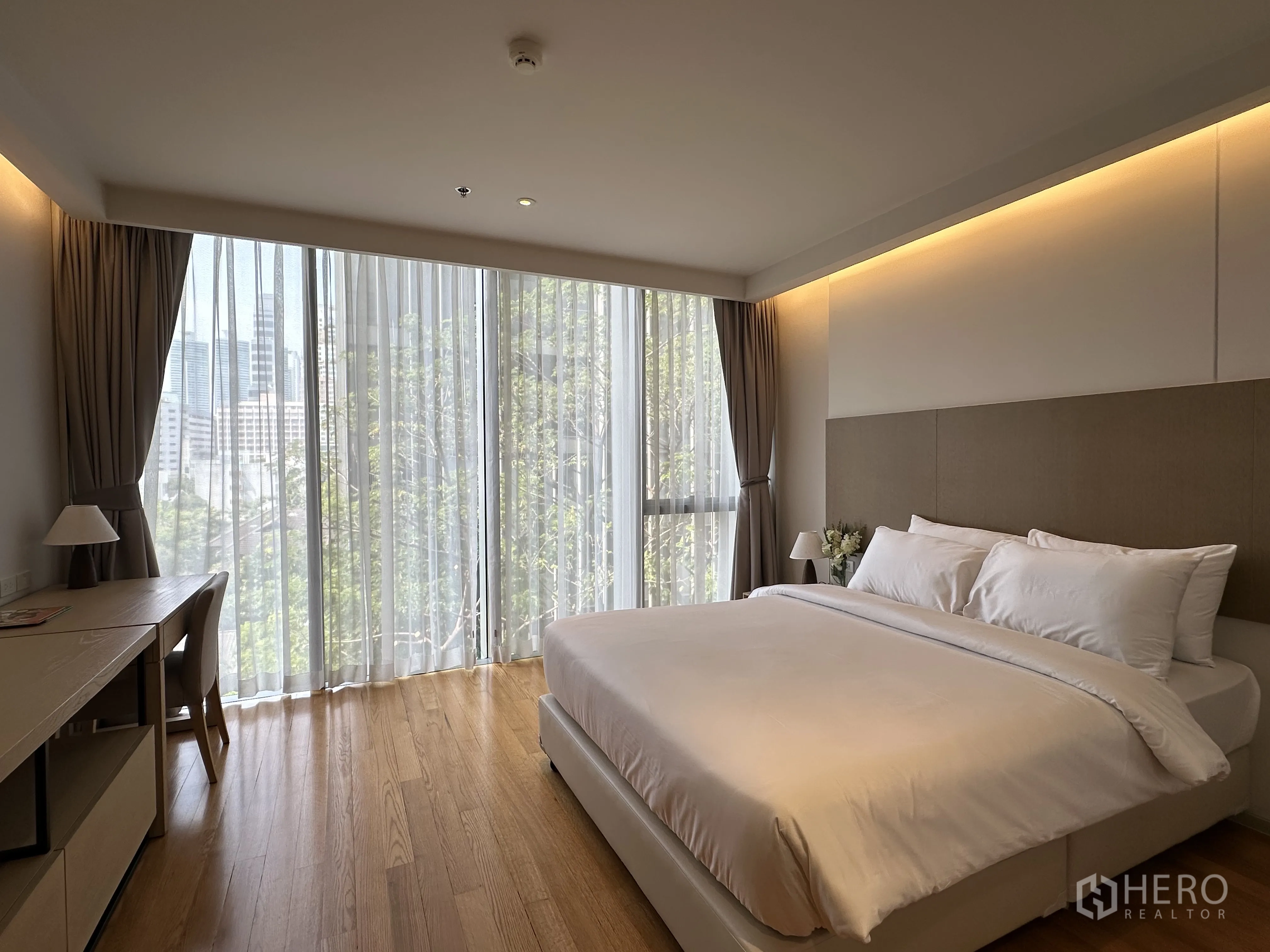 Condominium for rent in Khlong Toei, Bangkok - Second bedroom with large windows, work desk, and soft ambient lighting.