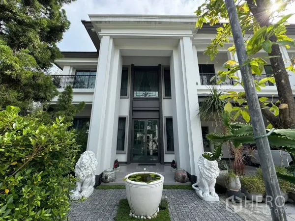 Detached House for sale in Mueang Pathum Thani, Pathum Thani - Grand entry with tall pillars, glass doors and lion statues flanking a garden urn.