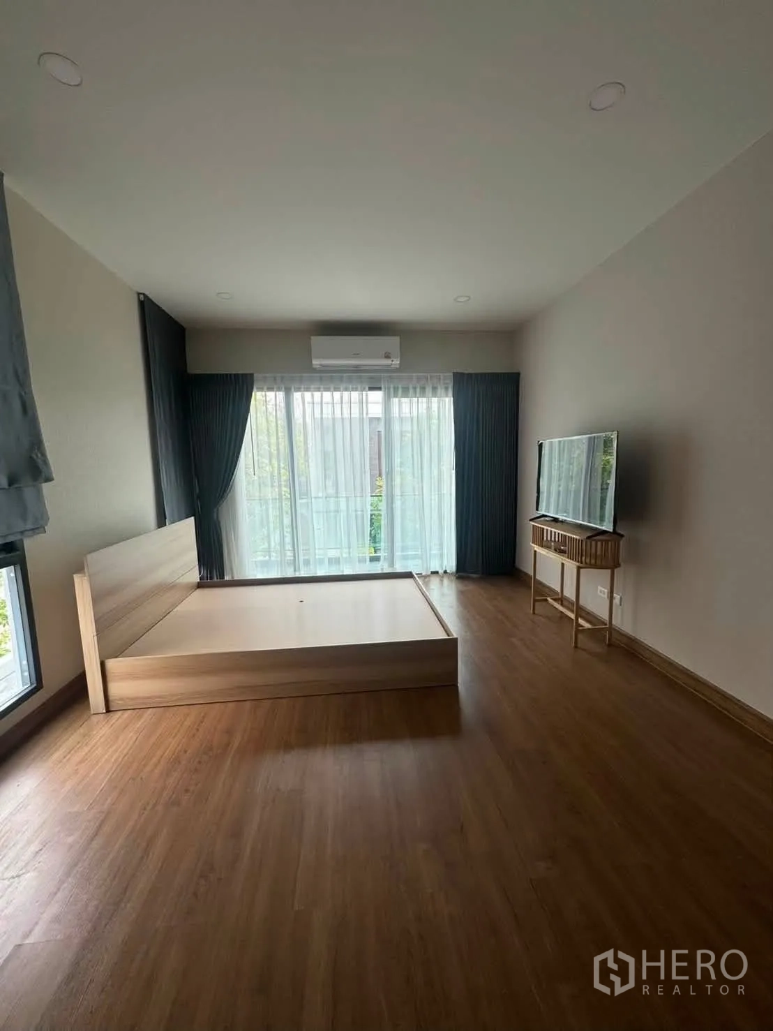 Detached House for rent or sale in Prawet, Bangkok - Large bedroom with bed frame, TV on console, floor-to-ceiling windows with curtains, and AC.