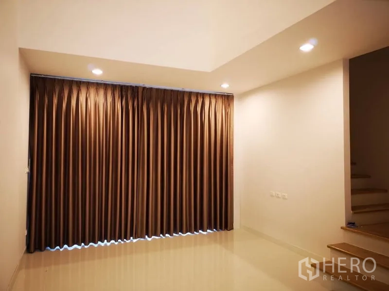 Townhouse for rent in Bang Na, Bangkok - Ground-floor room with full-length brown curtains, spotlights and staircase access