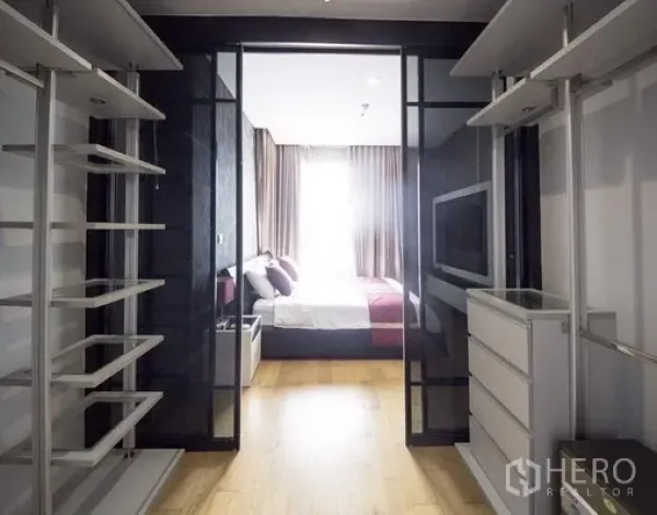 Condominium for rent in Khlong Toei, Bangkok - Glass-front walk-in closet with shelving and drawers leading to a sunlit bedroom in a Sukhumvit condominium.