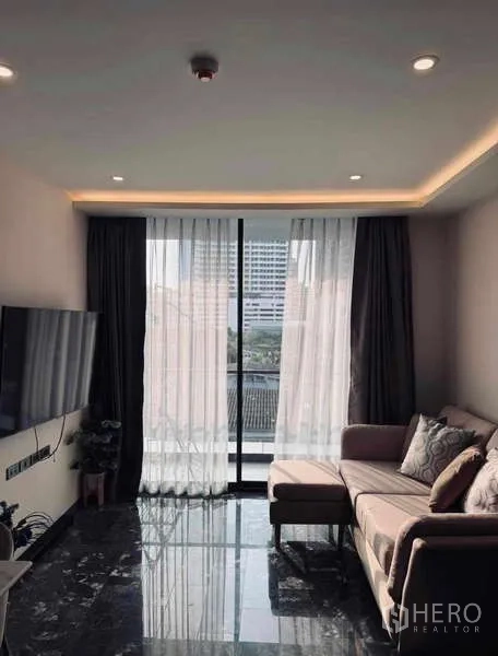 Condominium for rent in Khlong Toei, Bangkok - Bright living room with L-shaped sofa, TV and floor-to-ceiling window in Khlong Toei condo.