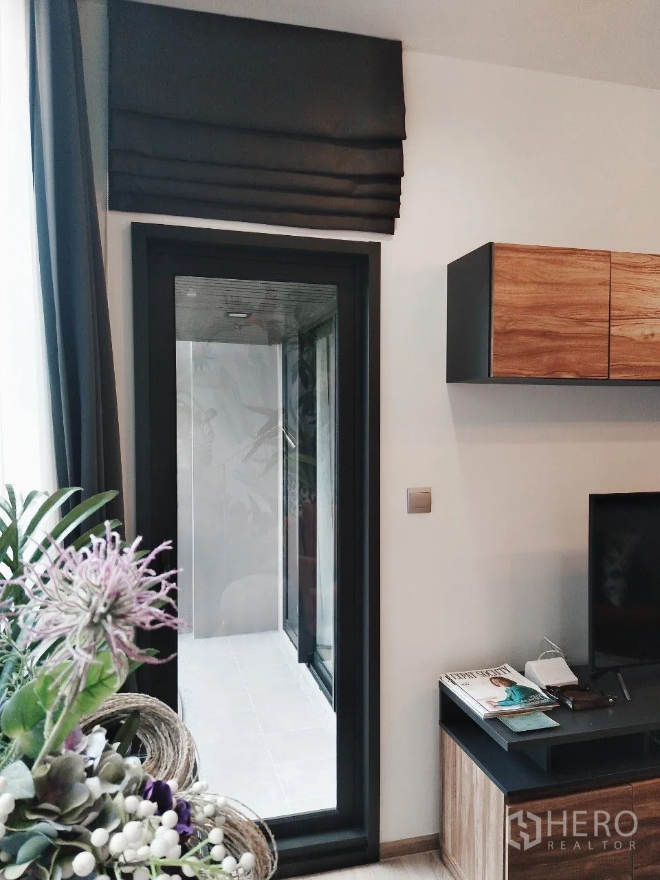 Condominium for rent in Watthana, Bangkok - Living area doorway to the balcony with roman shade and TV console nearby.