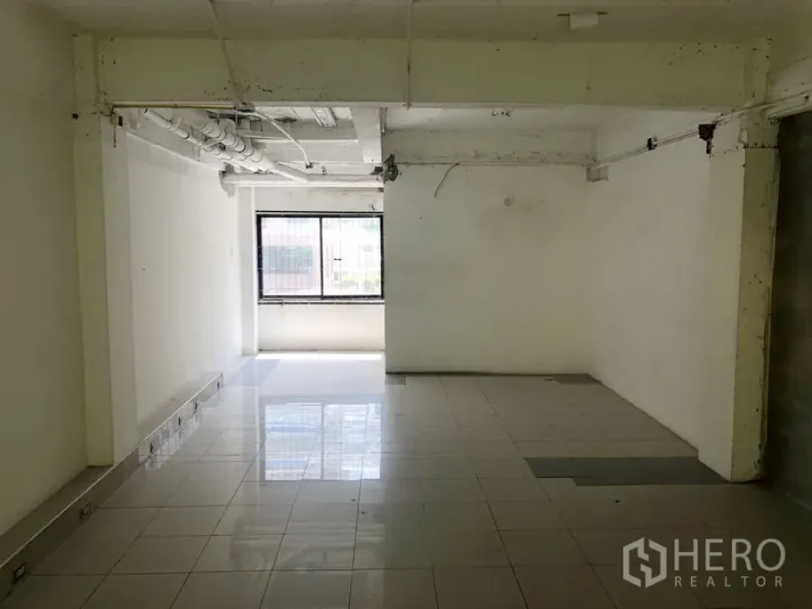 Retail Space for rent in Khlong Toei, Bangkok - Open-plan retail space with white walls, tiled flooring, exposed ceiling pipes and a bright window.