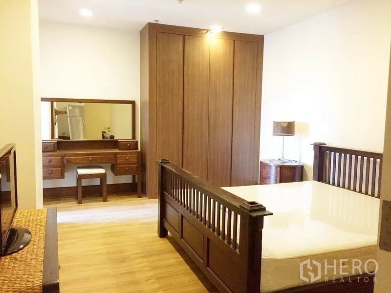 Condominium for rent in Khlong Toei, Bangkok - Second bedroom with large wardrobe, dressing table and warm lighting.