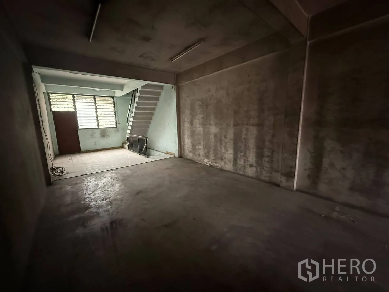 Shophouse for rent in Khlong Toei, Bangkok - Large room with concrete floor leading to a bright stair landing and window.
