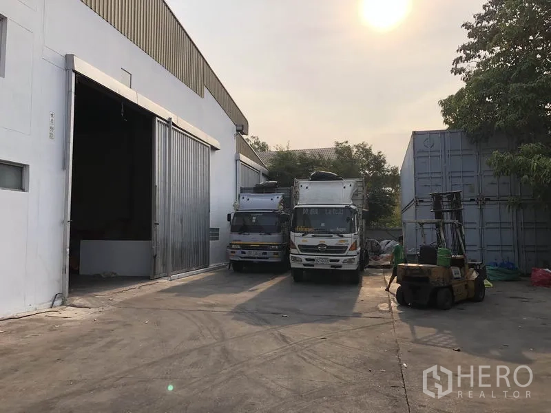 Factory for rent in Bang Bua Thong, Nonthaburi - Loading yard beside the factory with container trucks and forklift access in the afternoon light.