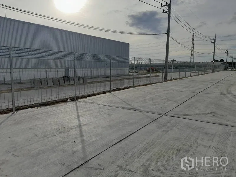 Factory for rent in Mueang Rayong, Rayong - Perimeter fencing along a concrete access road around the industrial site.