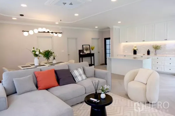 Detached House for sale in Bang Phli, Samut Prakan - Warm-toned lounge with sectional sofa, round coffee table and marble-top kitchen beyond