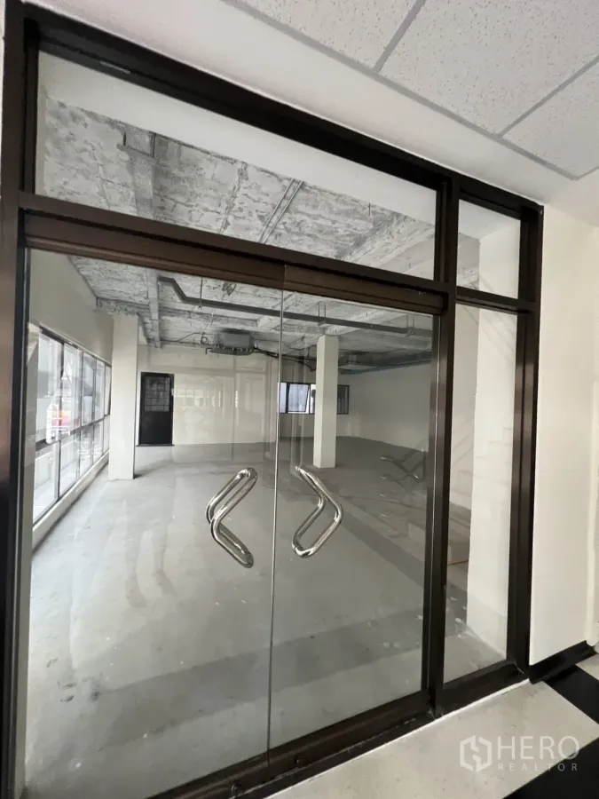 Retail Space for rent in Watthana, Bangkok - Glass double-door entrance to an open-plan retail unit with large windows and an unfinished ceiling.