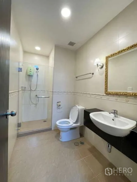 Apartment for rent in Khlong Toei, Bangkok - Second bathroom with glass shower, toilet and wall-mounted sink.