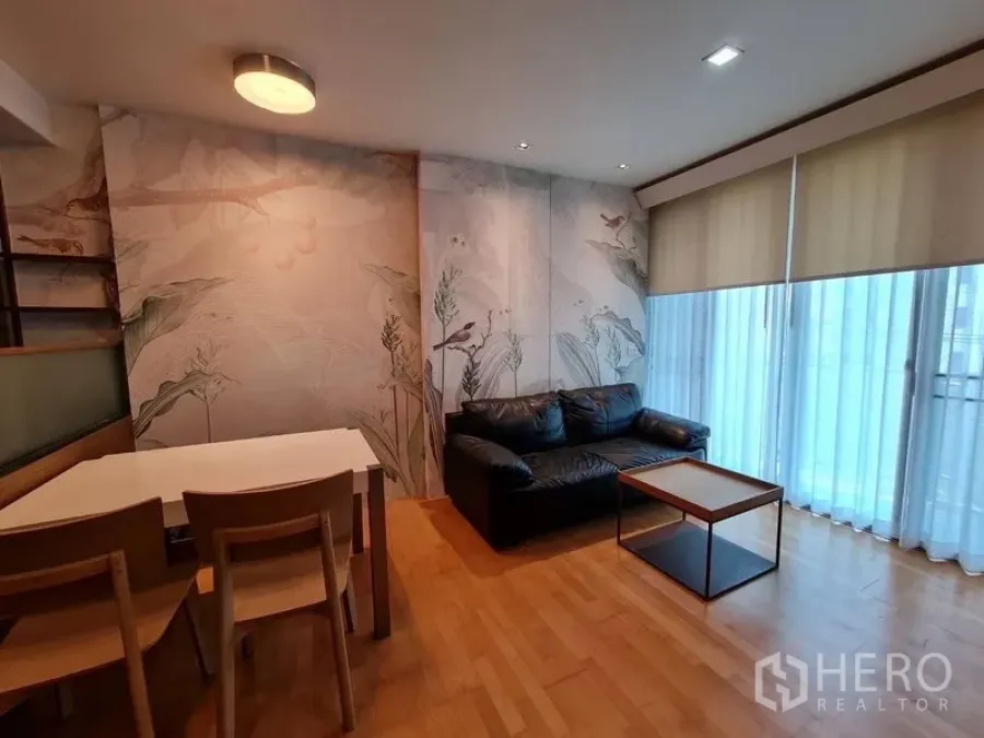 Condominium for sale in Khlong Toei, Bangkok - Bright living room with leather sofa, mural wallpaper and floor-to-ceiling windows with blinds.