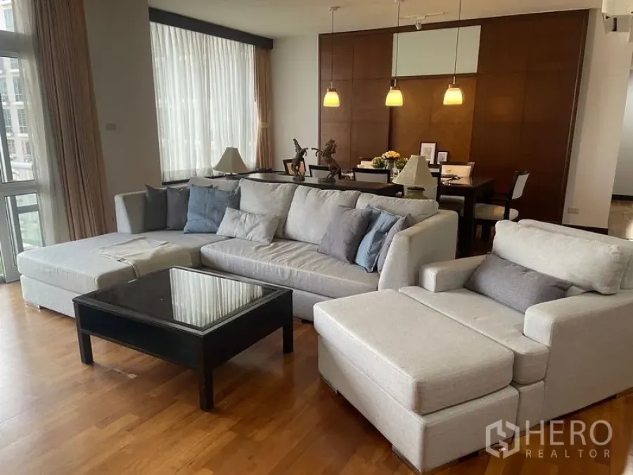 Condominium for rent in Pathum Wan, Bangkok - Spacious living room with grey L-shaped sofa, chaise and glass coffee table on hardwood floors.