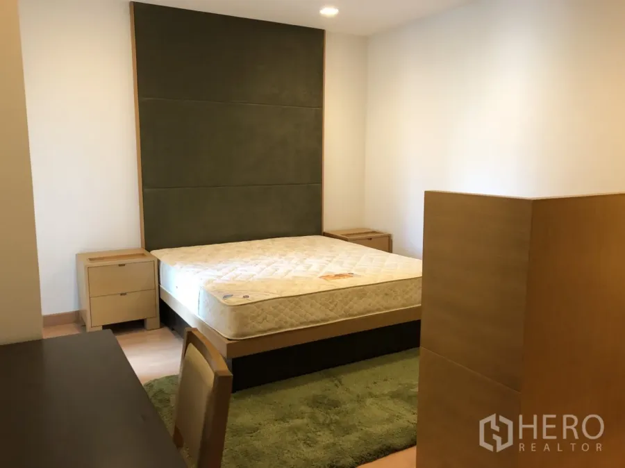 Condominium for rent in Khlong Toei, Bangkok - Bright master bedroom with padded headboard, bedside tables and a green rug in a Bangkok condo.