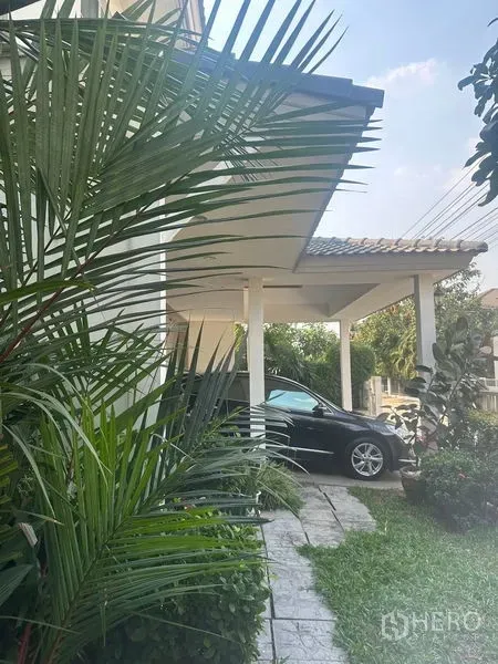 Detached House for rent in Bang Phli, Samut Prakan - Covered carport along the side of the house bordered by tropical plants.