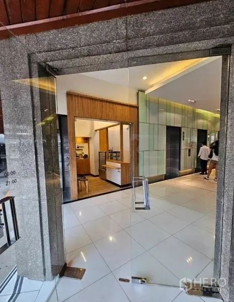 Retail Space for rent in Watthana, Bangkok - View through a glass entrance to a wood-accented retail kiosk beside elevator banks.