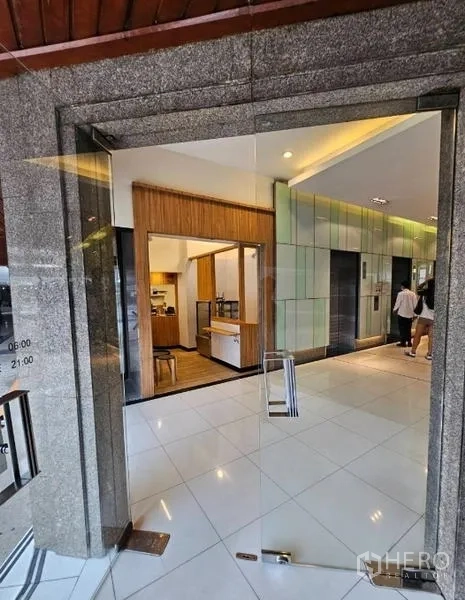 Retail Space for rent in Watthana, Bangkok - View through a glass entrance to a wood-accented retail kiosk beside elevator banks.