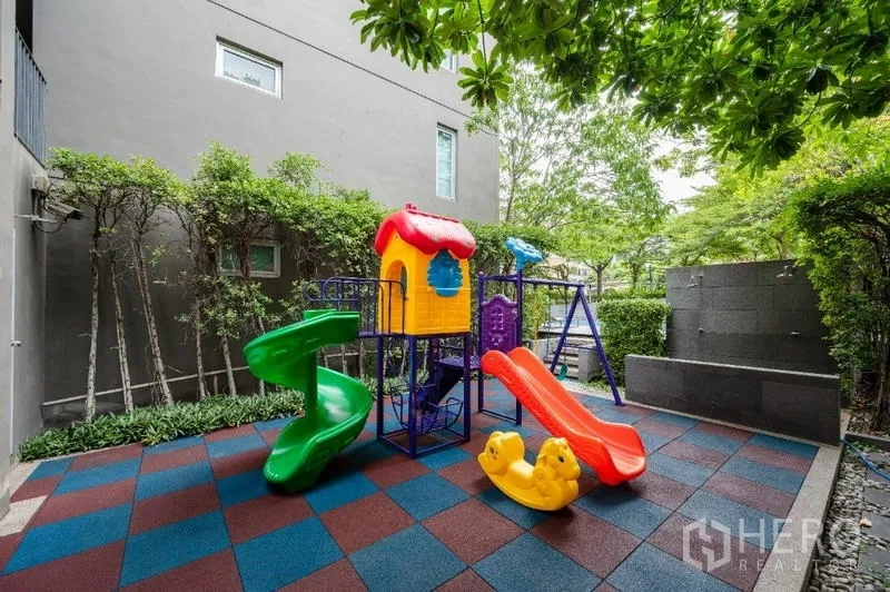 Condominium for sale - Outdoor playground with colorful slides and rubber safety flooring surrounded by greenery.