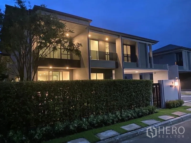 Detached House for rent in Bang Kapi, Bangkok - Evening view of contemporary house facade with warm lighting and tall privacy hedge.