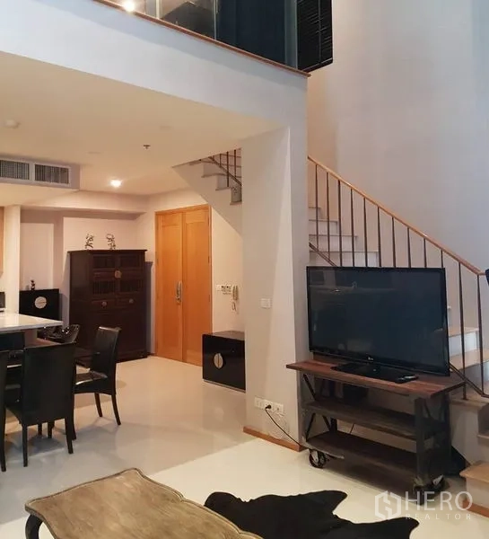 Condominium for rent or sale in Khlong Toei, Bangkok - Duplex living space with staircase, TV console and dining area.
