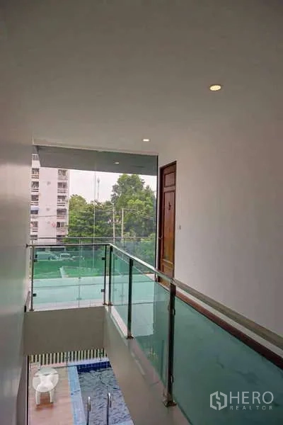 Detached House for sale in Lat Phrao, Bangkok - Upper corridor with glass balustrade overlooking the pool and surrounding neighborhood.
