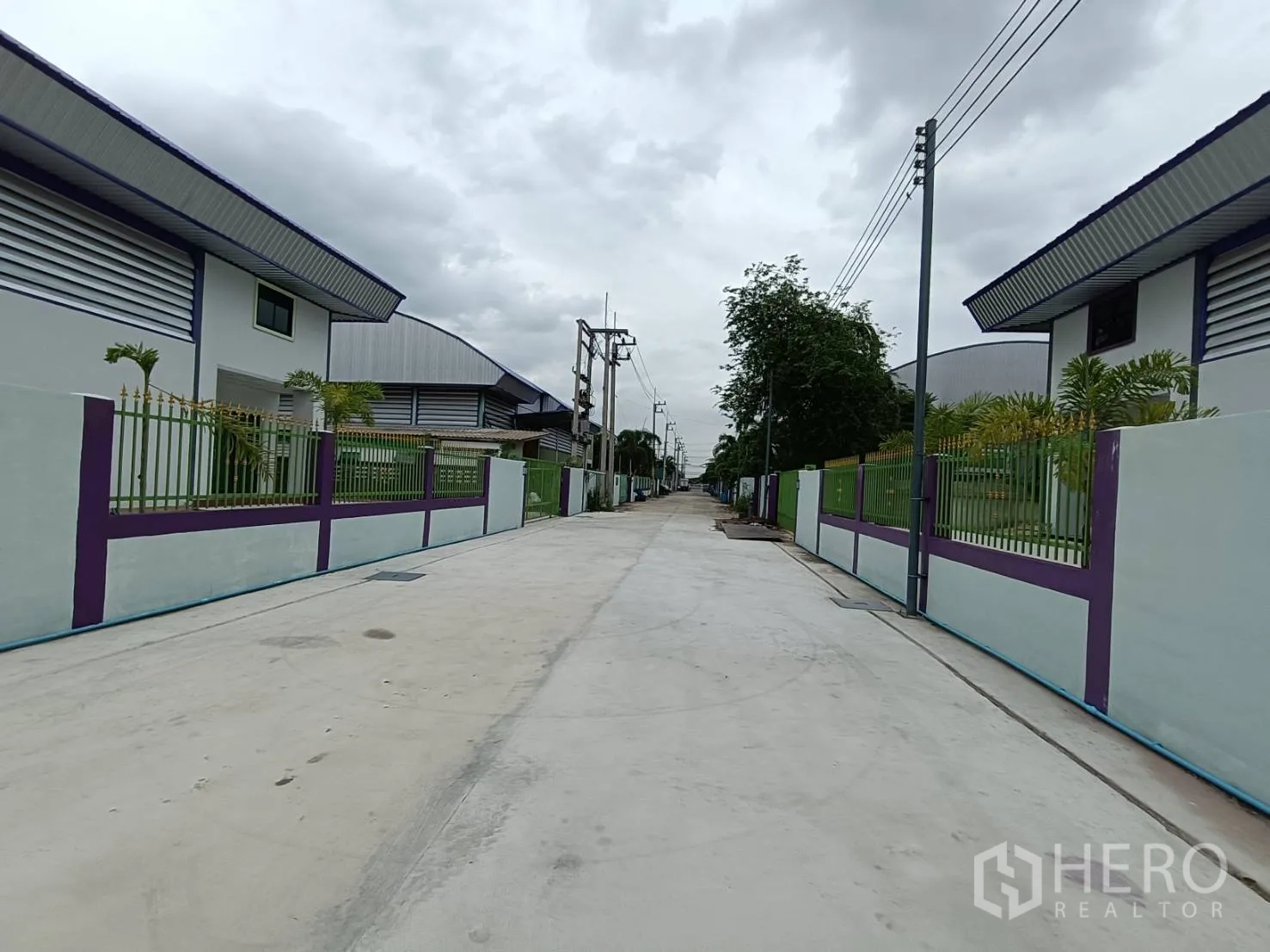 工厂 出租在Lam Luk Ka, Pathum Thani - 园区混凝土道路，两侧为带围栏的工厂与电线杆。