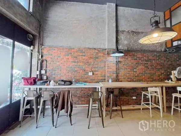 Retail Space for rent in Khlong Toei, Bangkok - Bar-height seating along an exposed brick wall under hanging lights beside the front windows.