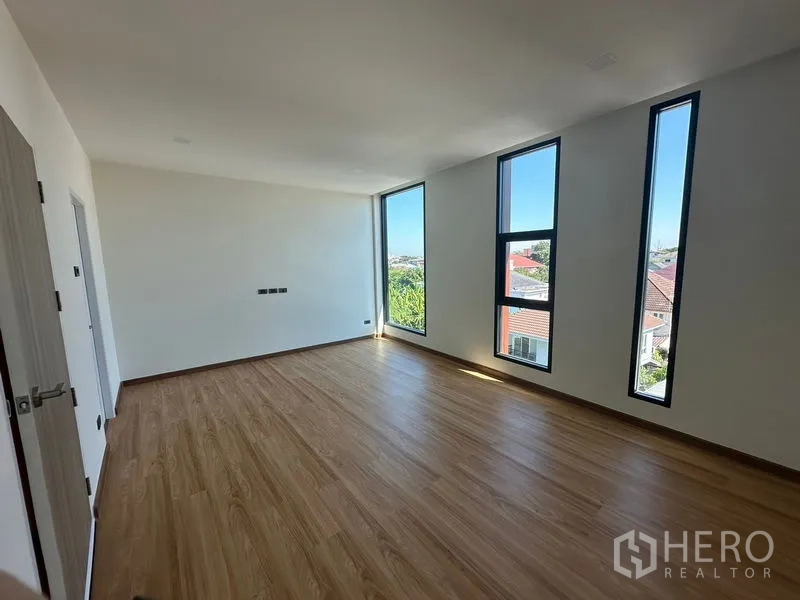Home Office for rent in Wang Thonglang, Bangkok - Large bedroom with slim vertical windows, wood flooring, and neighborhood views.